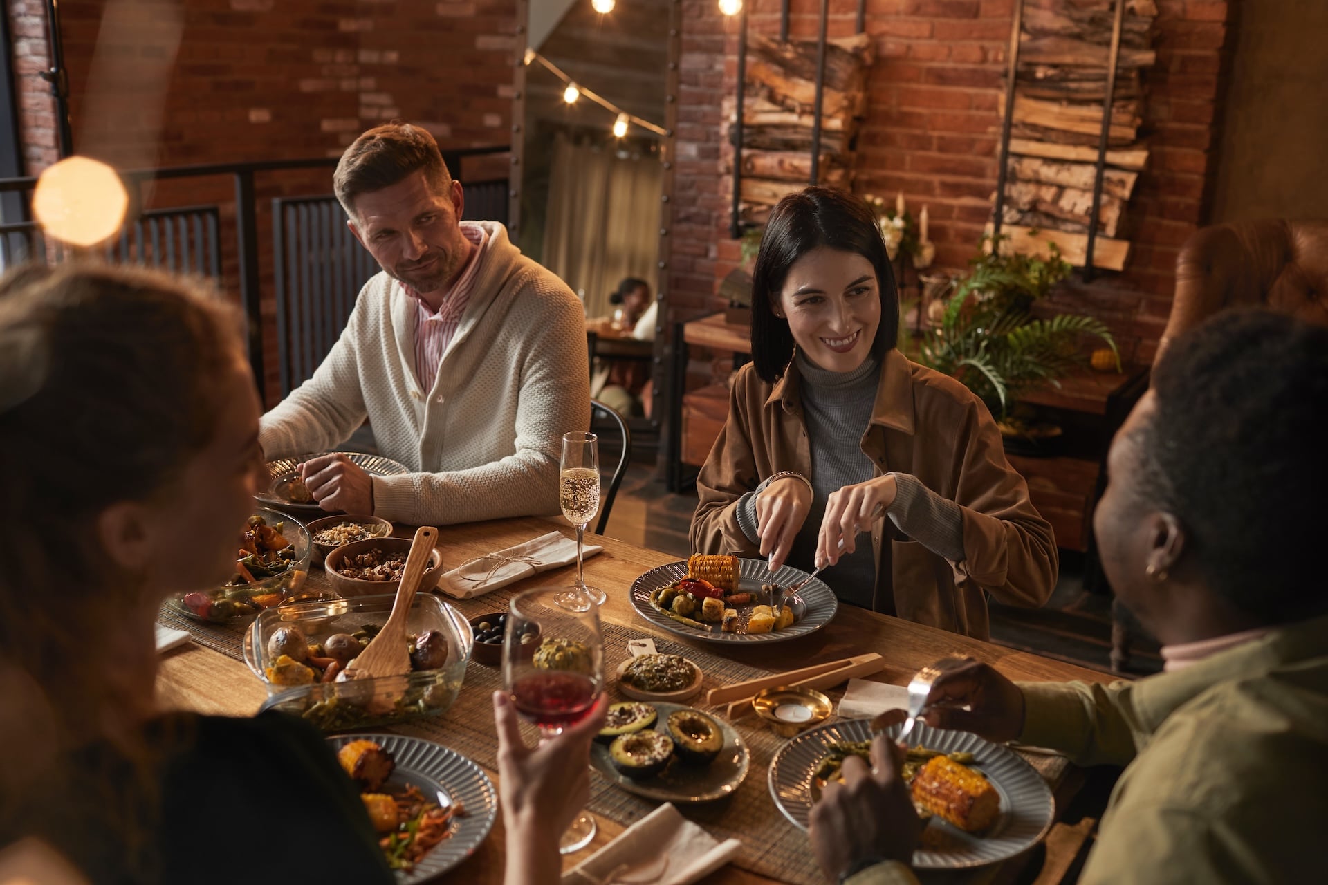 Group of friends sharing food and conversation at a cozy restaurant dinner table.
