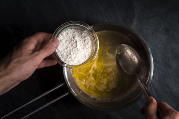 Chef pouring flour into melted butter to start a roux, the essential base of Cajun and Creole cuisine.