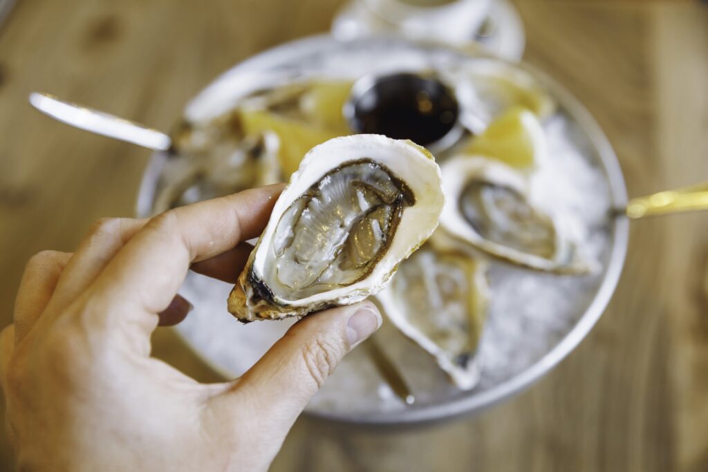 Hand holding a freshly shucked raw oyster served on ice in New Orleans