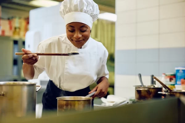 Chef tasting Cajun dish in a kitchen with pots and steam