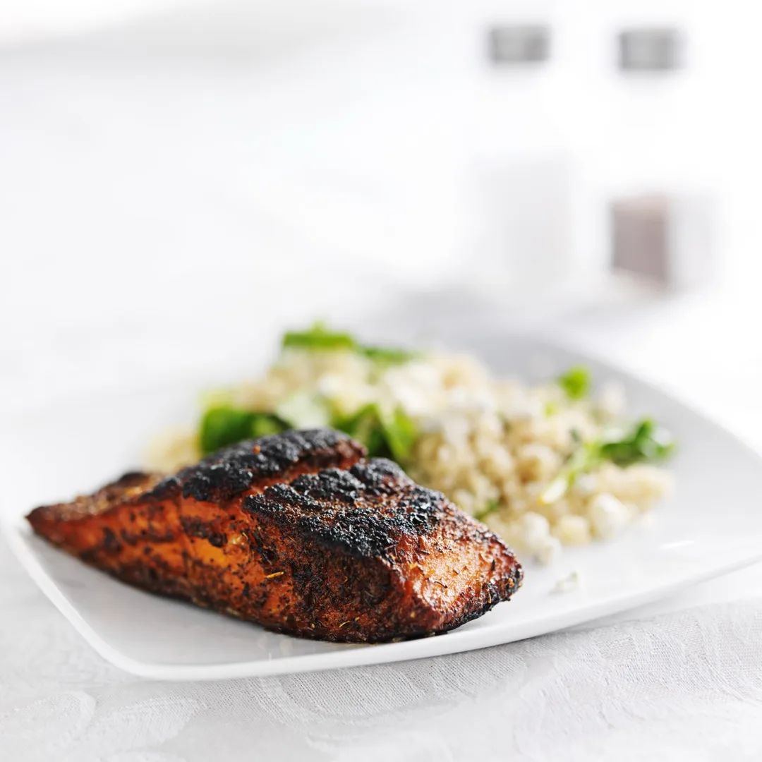 Blackened Gulf fish served with dirty rice and fresh lemon on a white plate