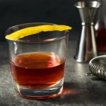 Classic Sazerac cocktail in a rocks glass with lemon peel on a dark bar counter