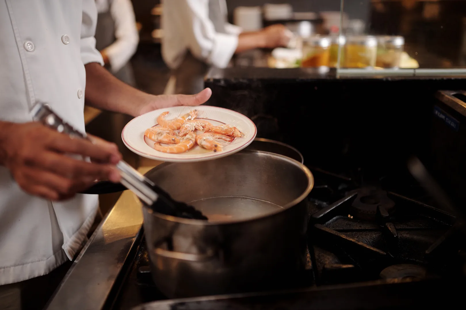 Chef plating boiled shrimp from a steaming pot in a professional kitchen