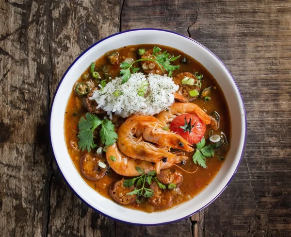 Seafood gumbo bowl with shrimp sausage rice and fresh herbs on rustic wooden table